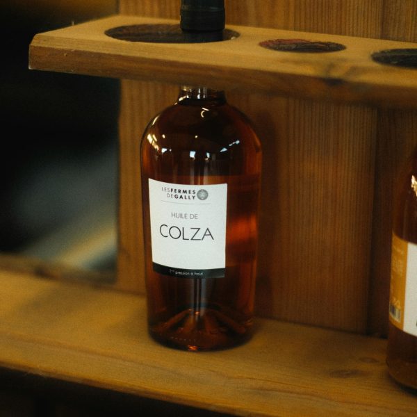 Close-up of a bottle labeled 'Huile de Colza' on a wooden shelf.