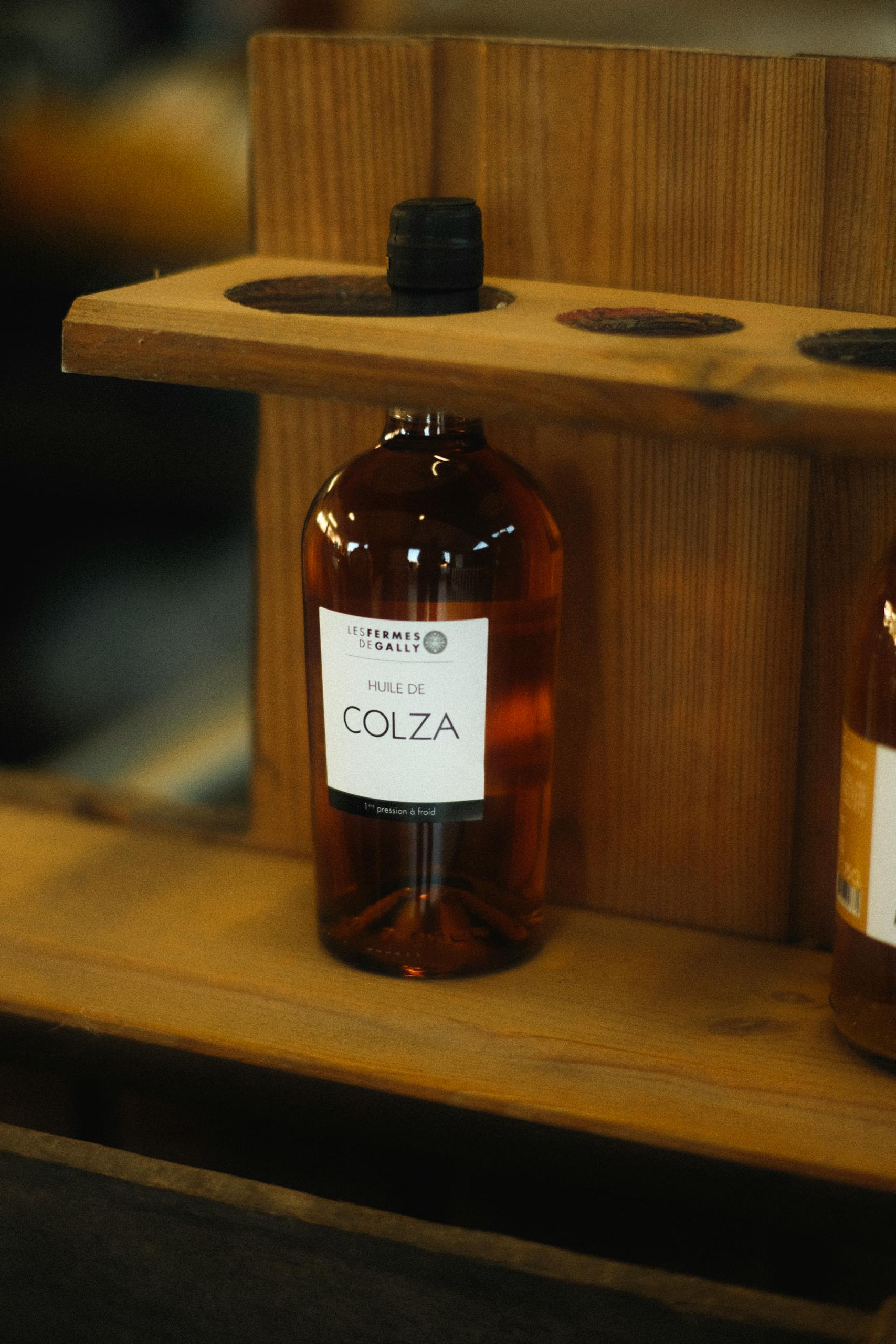 Photo par Mathias Reding Close-up of a bottle labeled 'Huile de Colza' on a wooden shelf.